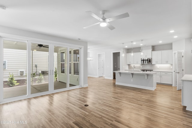 unfurnished living room featuring ceiling fan, sink, and light wood-type flooring