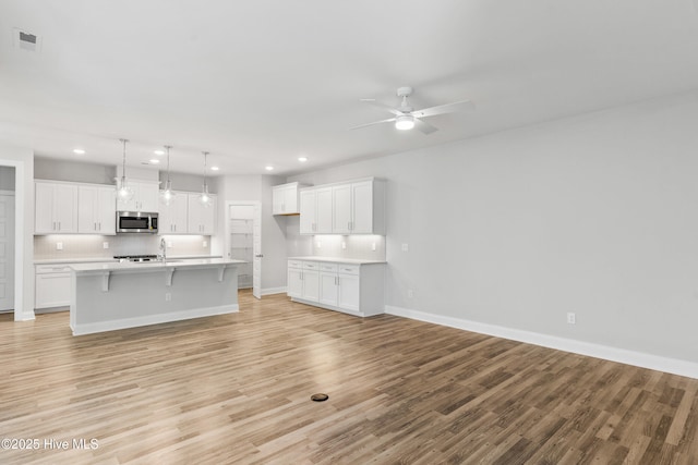 kitchen featuring white cabinetry, light wood-type flooring, an island with sink, and pendant lighting