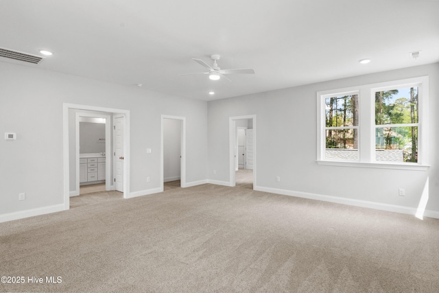 unfurnished bedroom with light carpet, ensuite bath, a walk in closet, and ceiling fan