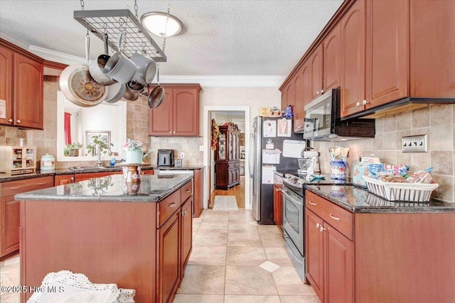 kitchen featuring a textured ceiling, appliances with stainless steel finishes, a kitchen island, dark stone counters, and crown molding