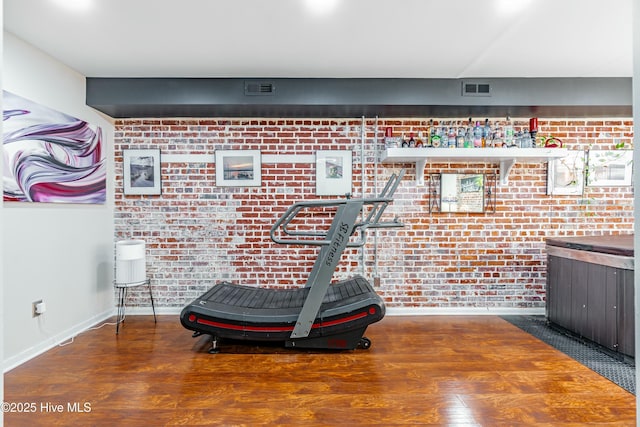 workout room featuring brick wall and dark hardwood / wood-style floors