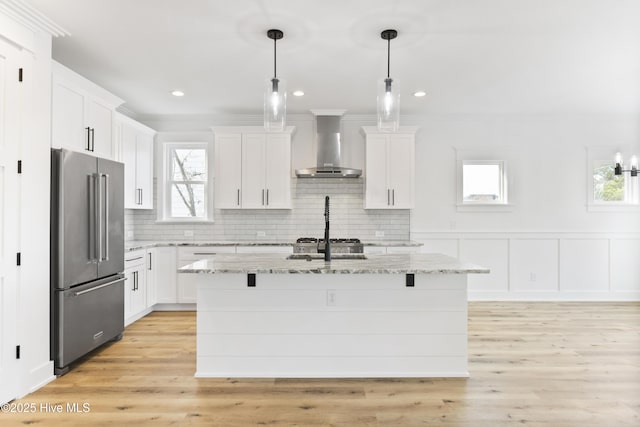 kitchen with white cabinets, wall chimney range hood, light stone counters, and high end fridge