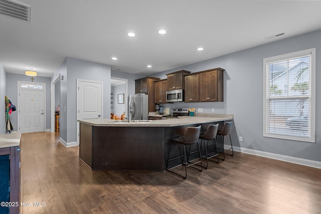 kitchen featuring dark brown cabinetry, a kitchen bar, dark hardwood / wood-style flooring, kitchen peninsula, and stainless steel appliances