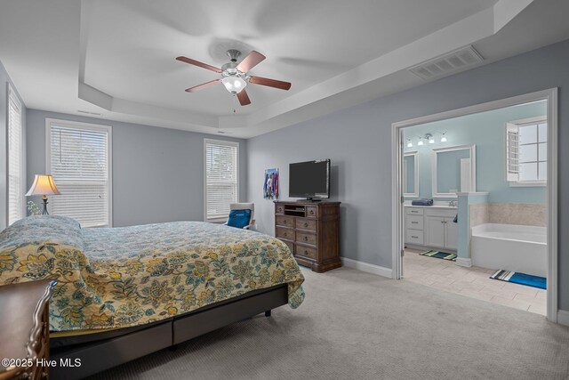 carpeted bedroom with ceiling fan, connected bathroom, and a tray ceiling