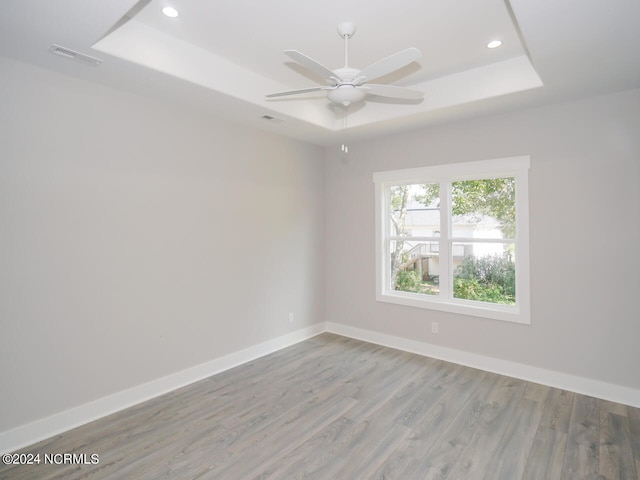 unfurnished room with light hardwood / wood-style floors, a tray ceiling, and ceiling fan