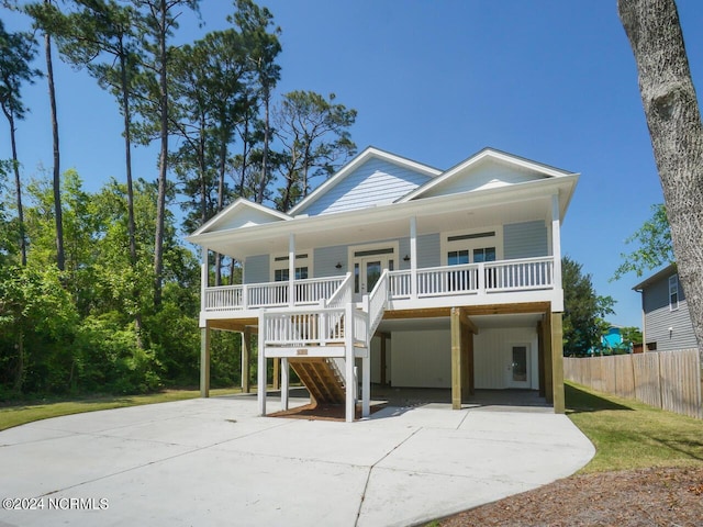 beach home featuring fence, driveway, a porch, stairs, and a carport