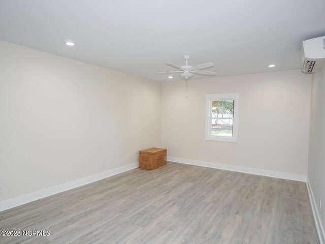 unfurnished room with light wood-type flooring, an AC wall unit, and ceiling fan