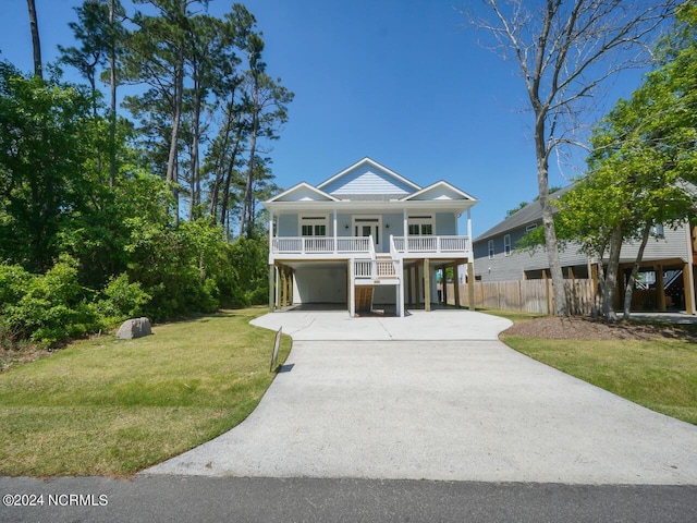 coastal home featuring a carport, concrete driveway, covered porch, and a front yard