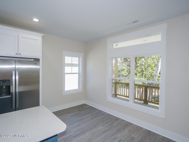 kitchen featuring wood finished floors, baseboards, light countertops, white cabinets, and stainless steel refrigerator with ice dispenser