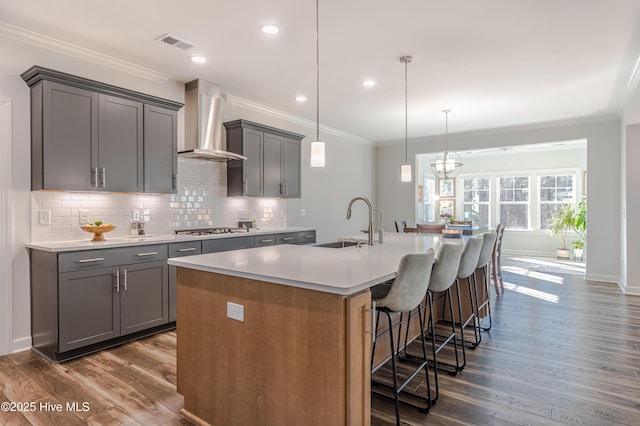 kitchen featuring decorative light fixtures, wall chimney range hood, sink, a kitchen island with sink, and stainless steel gas cooktop