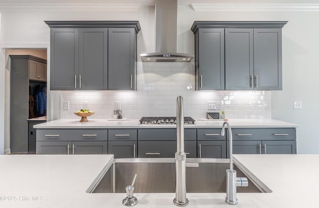 kitchen featuring wall chimney range hood, tasteful backsplash, ornamental molding, stainless steel gas stovetop, and gray cabinetry