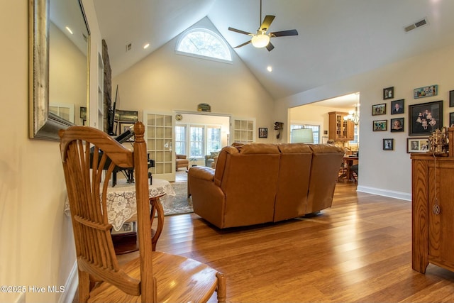 living room with wood-type flooring, ceiling fan with notable chandelier, and high vaulted ceiling