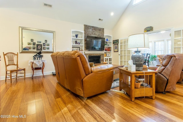 living room featuring light hardwood / wood-style flooring, built in shelves, a fireplace, and high vaulted ceiling