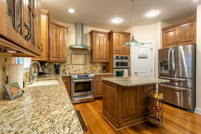 kitchen featuring sink, appliances with stainless steel finishes, light stone counters, a kitchen island, and wall chimney exhaust hood