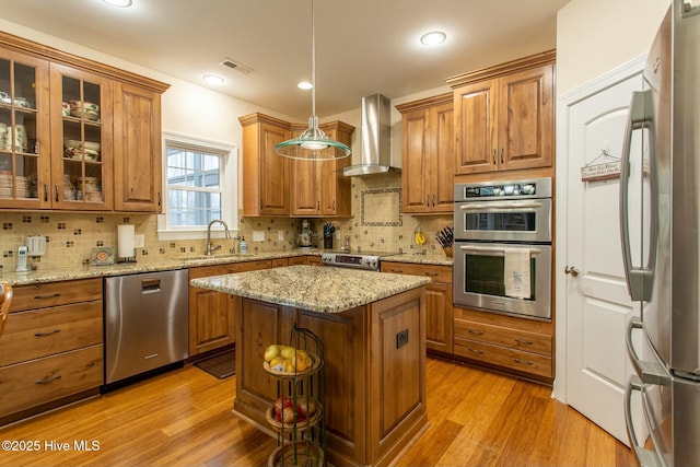 kitchen with sink, hanging light fixtures, stainless steel appliances, a kitchen island, and wall chimney exhaust hood