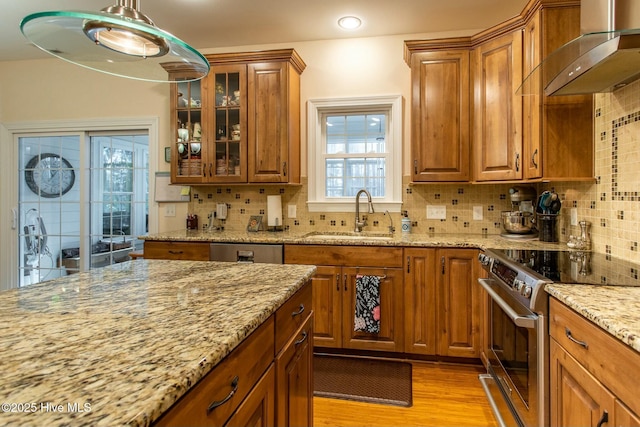 kitchen with wall chimney exhaust hood, sink, light stone counters, appliances with stainless steel finishes, and pendant lighting