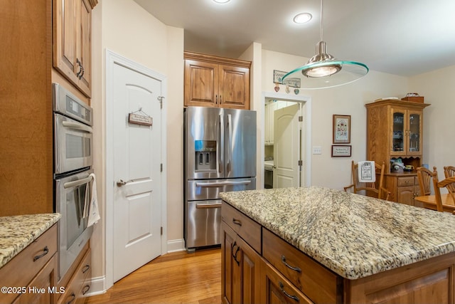 kitchen with light stone counters, a center island, light hardwood / wood-style flooring, appliances with stainless steel finishes, and pendant lighting