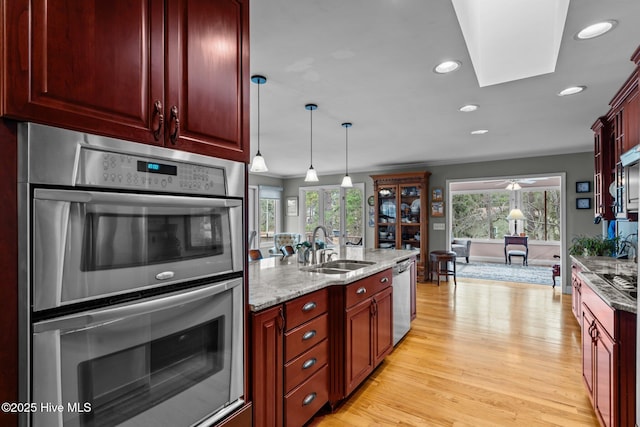 kitchen with stainless steel appliances, a sink, a healthy amount of sunlight, light stone countertops, and reddish brown cabinets