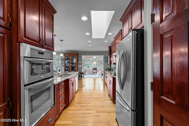 kitchen featuring light stone counters, stainless steel appliances, a sink, light wood-style floors, and dark brown cabinets