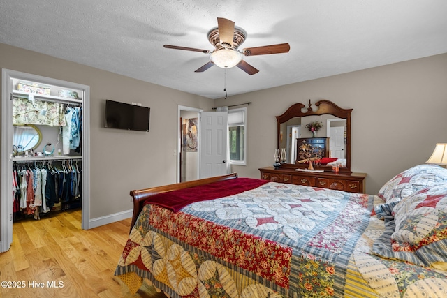 bedroom with a textured ceiling, baseboards, a closet, light wood-type flooring, and a walk in closet