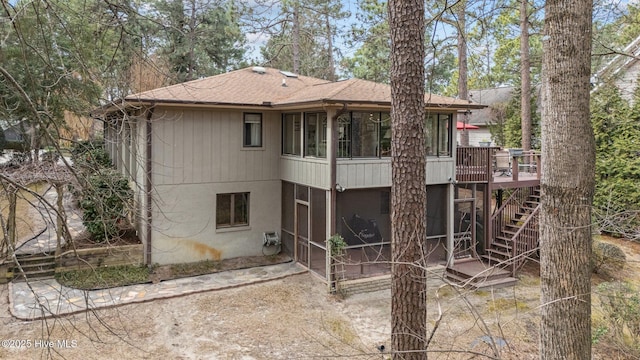 rear view of house featuring a deck, a sunroom, roof with shingles, and stairway