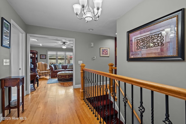 corridor featuring a chandelier, baseboards, an upstairs landing, and light wood-style floors