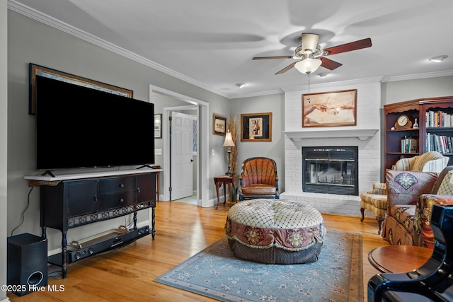 living room featuring ornamental molding, a fireplace, light wood-style flooring, and a ceiling fan