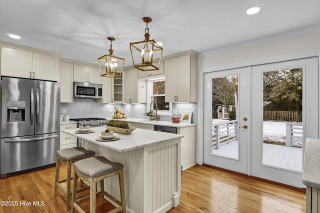 kitchen with hanging light fixtures, stainless steel appliances, light hardwood / wood-style floors, a kitchen island, and french doors