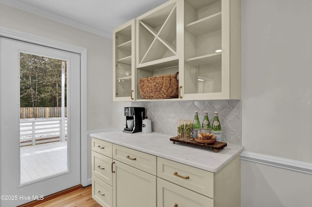 bar featuring tasteful backsplash, ornamental molding, and light hardwood / wood-style floors