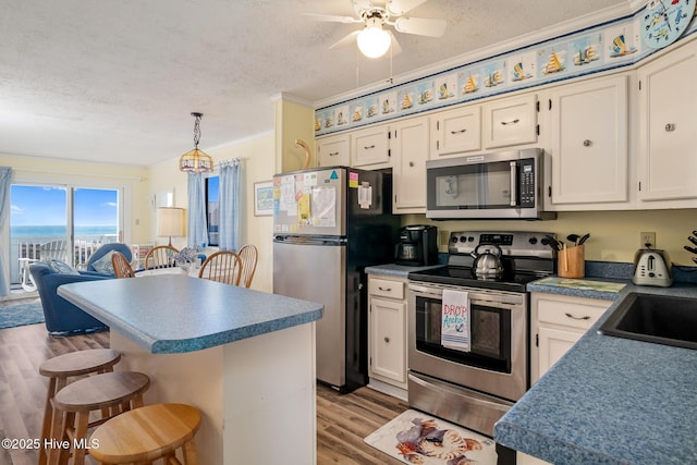 kitchen with a kitchen bar, hanging light fixtures, stainless steel appliances, a textured ceiling, and light hardwood / wood-style flooring