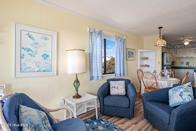 living room with sink, ceiling fan, light hardwood / wood-style floors, crown molding, and a textured ceiling