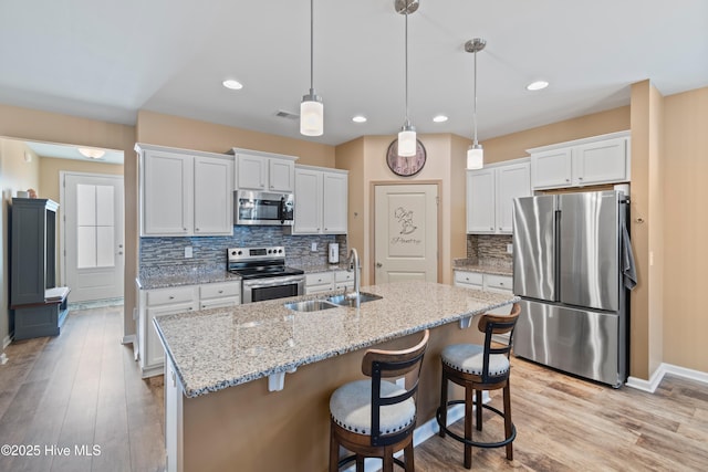 kitchen with appliances with stainless steel finishes, sink, white cabinetry, and decorative light fixtures