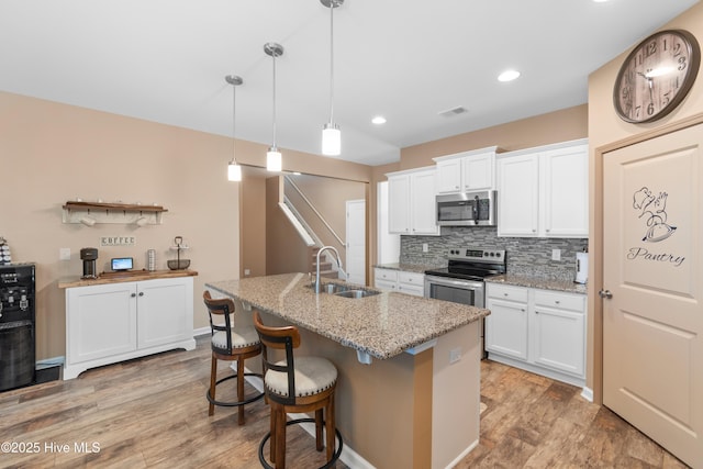 kitchen featuring hanging light fixtures, white cabinets, stainless steel appliances, and an island with sink