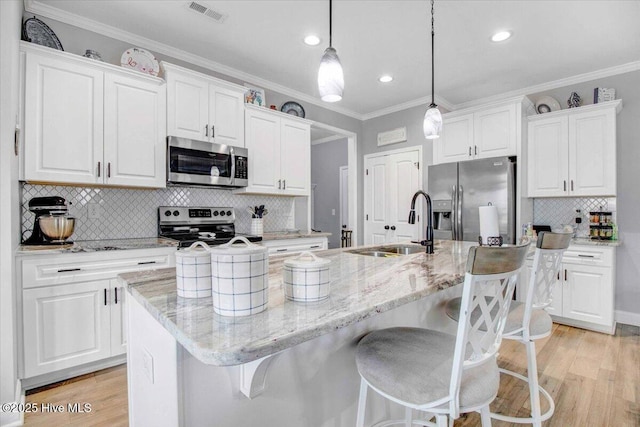 kitchen with decorative light fixtures, white cabinetry, stainless steel appliances, and an island with sink