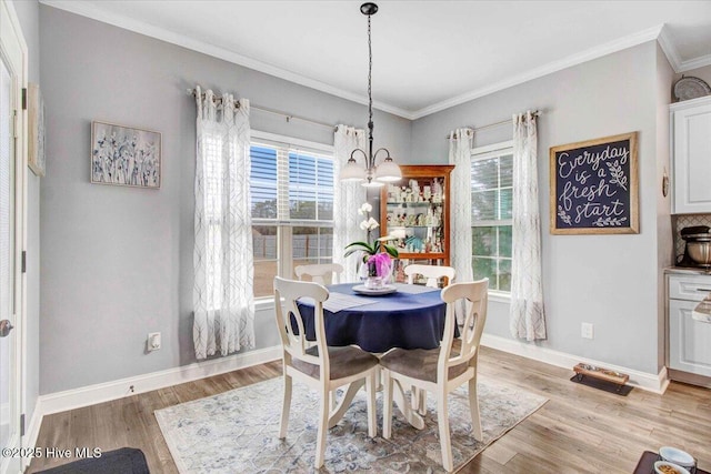 dining area with light wood-type flooring, a notable chandelier, a wealth of natural light, and crown molding