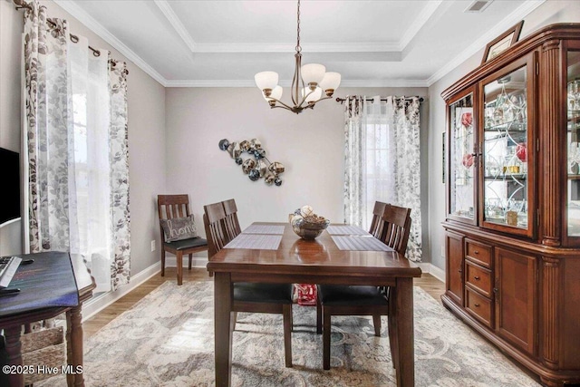 dining space with a raised ceiling, light wood-type flooring, crown molding, and an inviting chandelier