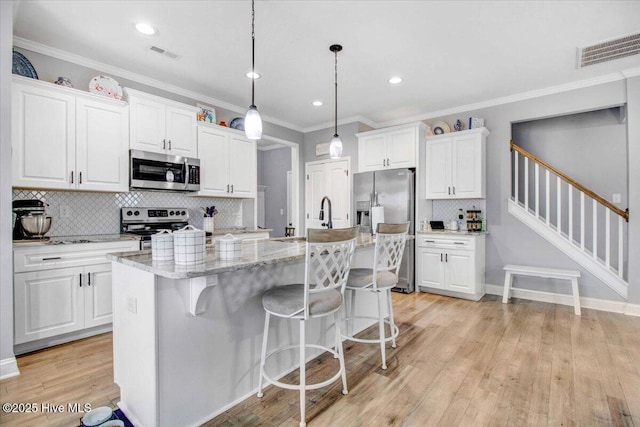 kitchen with light stone countertops, pendant lighting, white cabinets, stainless steel appliances, and a center island with sink