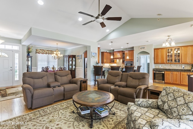 living room with ceiling fan with notable chandelier, light hardwood / wood-style flooring, high vaulted ceiling, and wine cooler