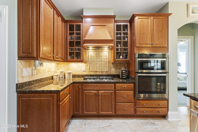 kitchen with custom exhaust hood, appliances with stainless steel finishes, dark stone countertops, and tasteful backsplash