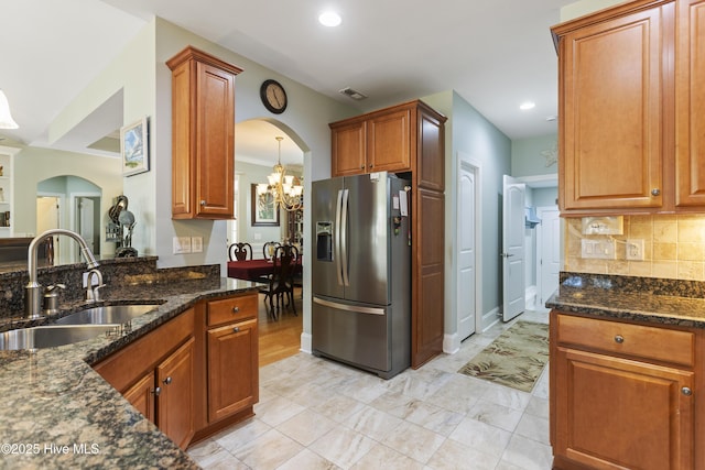 kitchen featuring stainless steel refrigerator with ice dispenser, sink, a chandelier, and dark stone countertops