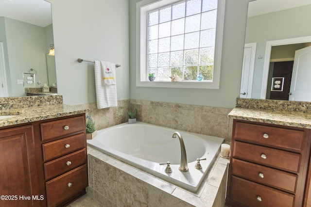 bathroom with tiled bath, plenty of natural light, and vanity