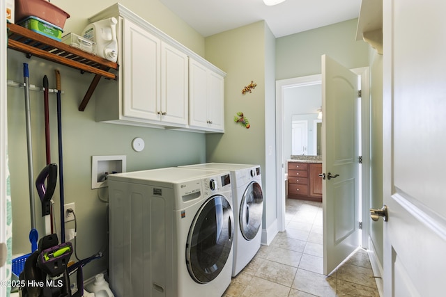 clothes washing area featuring light tile patterned floors, washer and clothes dryer, and cabinets