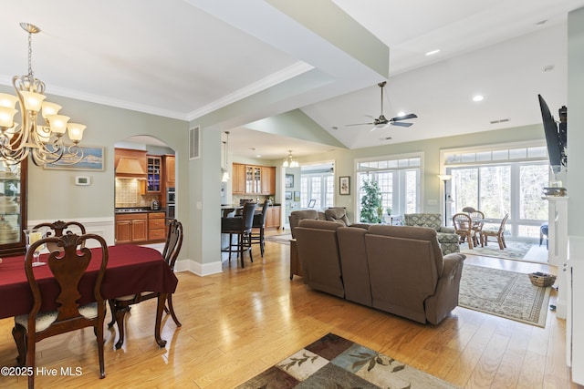 living room with vaulted ceiling, ornamental molding, ceiling fan with notable chandelier, and light hardwood / wood-style flooring