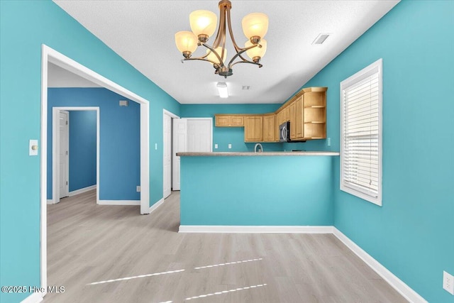 kitchen with kitchen peninsula, a textured ceiling, hanging light fixtures, and light brown cabinets