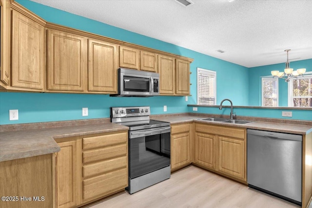 kitchen with sink, light hardwood / wood-style flooring, appliances with stainless steel finishes, an inviting chandelier, and a textured ceiling