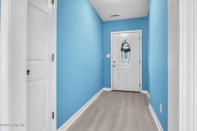 doorway with a textured ceiling and light hardwood / wood-style flooring