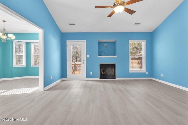 unfurnished living room with plenty of natural light, ceiling fan with notable chandelier, and light hardwood / wood-style flooring