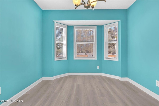 empty room with a notable chandelier, a healthy amount of sunlight, and light wood-type flooring