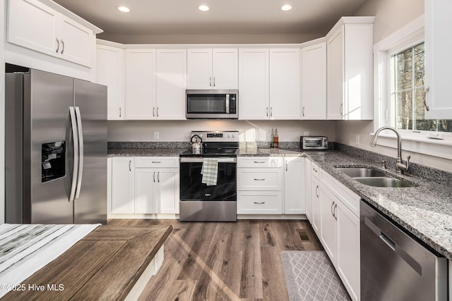 kitchen with sink, appliances with stainless steel finishes, white cabinetry, dark stone countertops, and dark hardwood / wood-style flooring