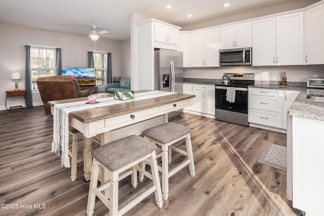 kitchen featuring white cabinetry, appliances with stainless steel finishes, a kitchen bar, and dark hardwood / wood-style flooring